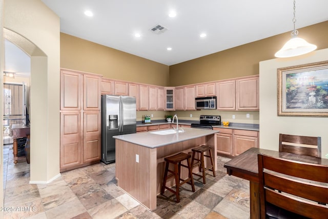 kitchen with a kitchen island with sink, stainless steel appliances, a sink, light countertops, and glass insert cabinets