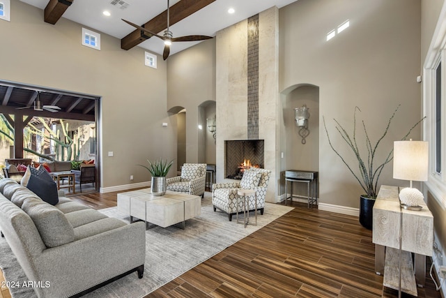 living room with beam ceiling, ceiling fan, a fireplace, and a towering ceiling