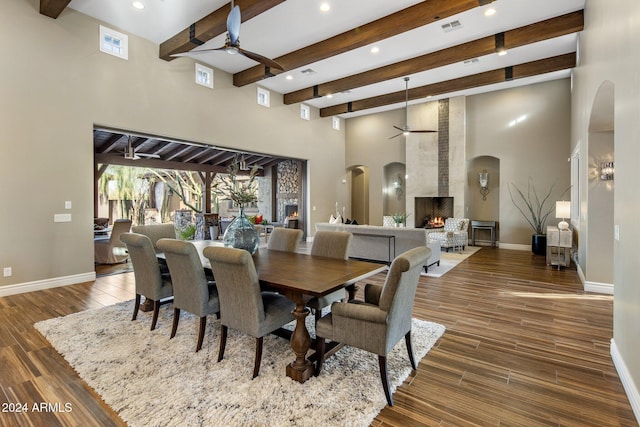 dining area featuring beam ceiling, a large fireplace, ceiling fan, and a high ceiling