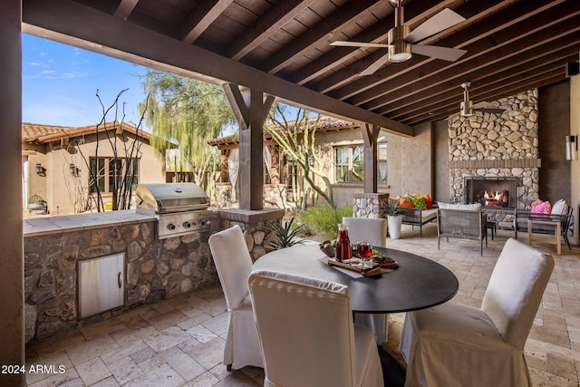 view of patio / terrace with an outdoor living space with a fireplace, area for grilling, ceiling fan, and an outdoor kitchen