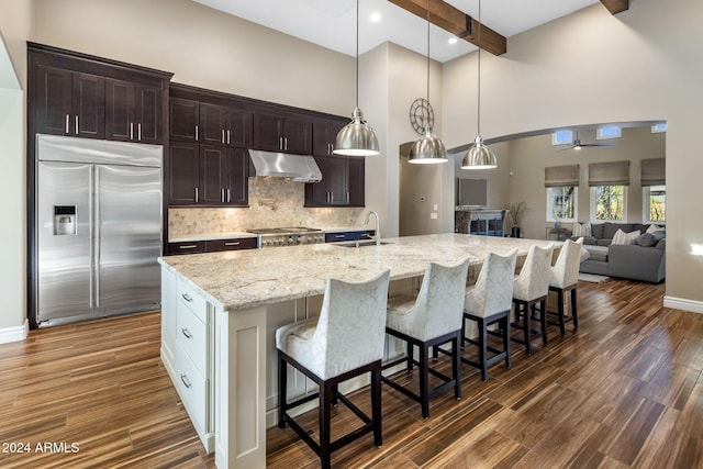 kitchen with sink, built in fridge, beamed ceiling, a breakfast bar area, and a center island with sink