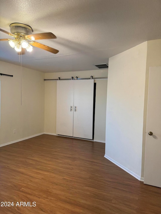 unfurnished bedroom with dark hardwood / wood-style flooring, a barn door, ceiling fan, and a textured ceiling