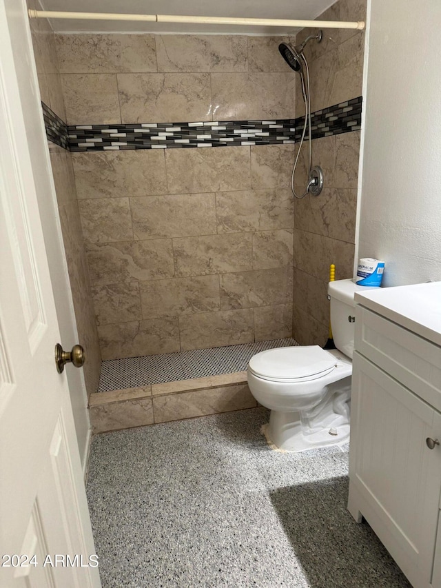 bathroom featuring a tile shower, vanity, and toilet