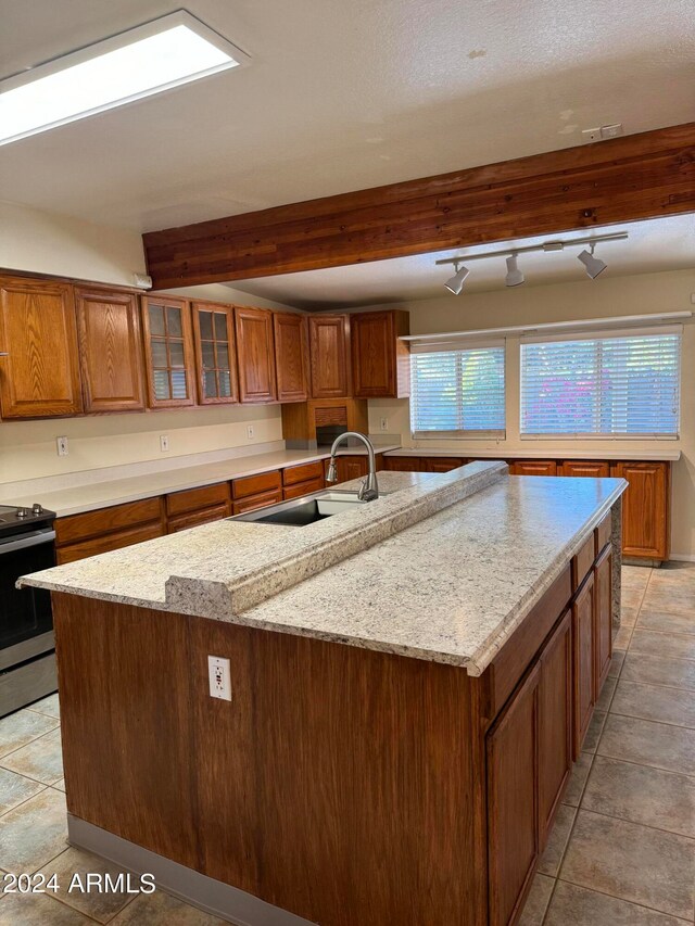 kitchen with electric range, light tile flooring, a center island with sink, and track lighting