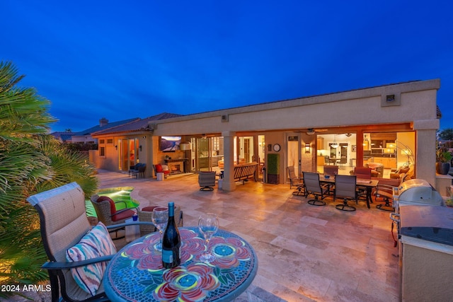 patio terrace at dusk featuring ceiling fan and exterior kitchen