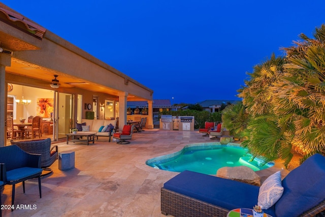 pool at night with outdoor lounge area, a patio, ceiling fan, and exterior kitchen