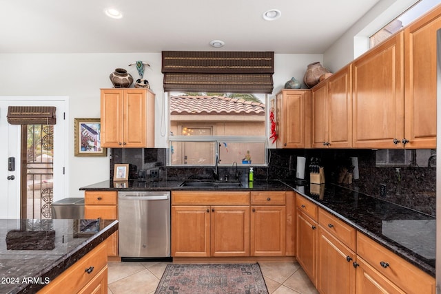 kitchen with light tile patterned floors, stainless steel dishwasher, dark stone counters, and sink