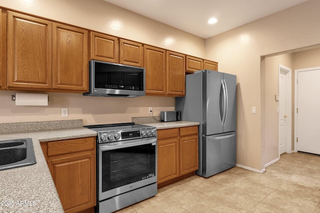 kitchen featuring light countertops, appliances with stainless steel finishes, a sink, and brown cabinets