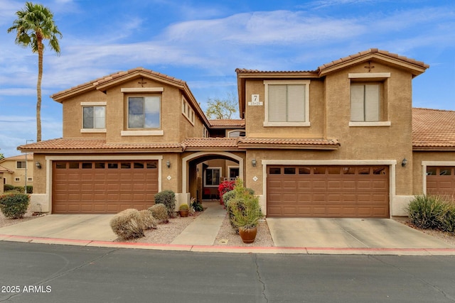 mediterranean / spanish home with a garage, driveway, a tiled roof, and stucco siding