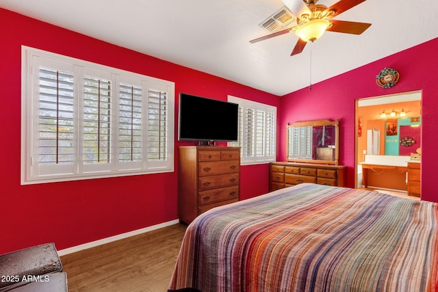 bedroom featuring lofted ceiling, ensuite bathroom, wood finished floors, visible vents, and baseboards