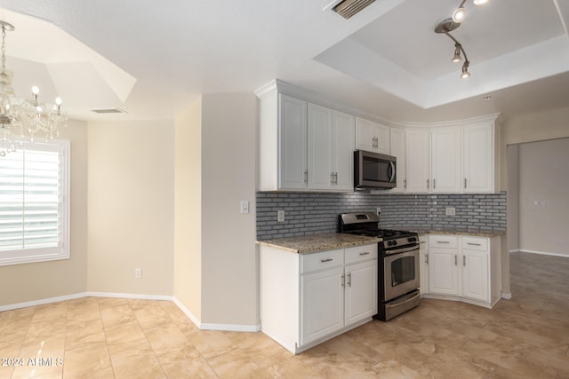 kitchen with decorative backsplash, appliances with stainless steel finishes, a notable chandelier, light stone counters, and white cabinetry