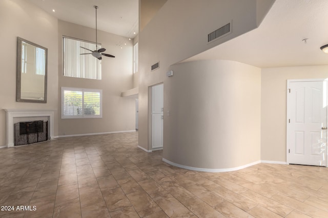 unfurnished living room featuring ceiling fan and a high ceiling