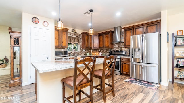 kitchen with appliances with stainless steel finishes, light wood-type flooring, light stone counters, wall chimney range hood, and a kitchen island