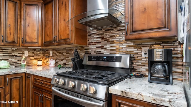 kitchen with stainless steel gas range, backsplash, light stone counters, and exhaust hood