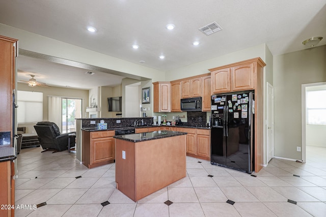 kitchen featuring dark stone counters, a center island, light tile patterned flooring, black appliances, and ceiling fan