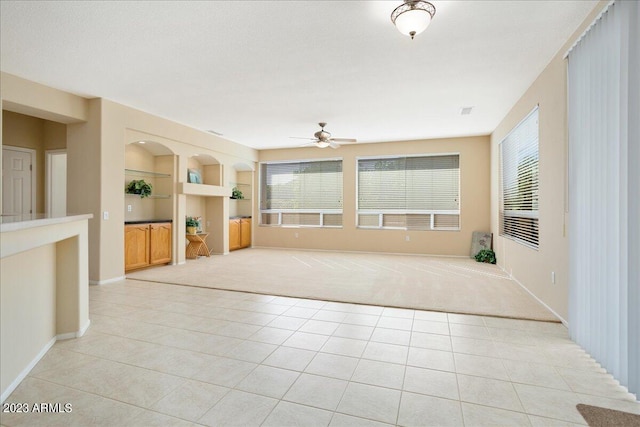 unfurnished living room with ceiling fan, built in features, and light tile patterned floors