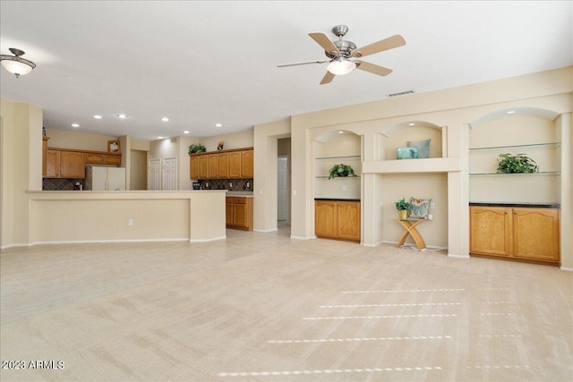 unfurnished living room featuring light carpet, built in features, and ceiling fan