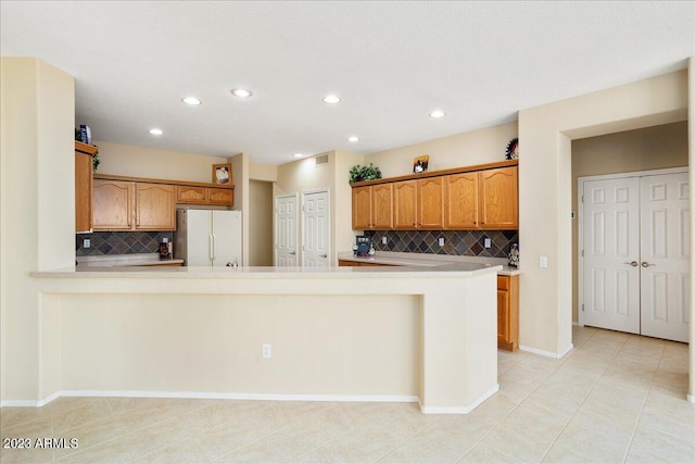 kitchen with white fridge, backsplash, light tile patterned floors, and kitchen peninsula