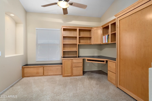 unfurnished office featuring light carpet, lofted ceiling, built in desk, and ceiling fan