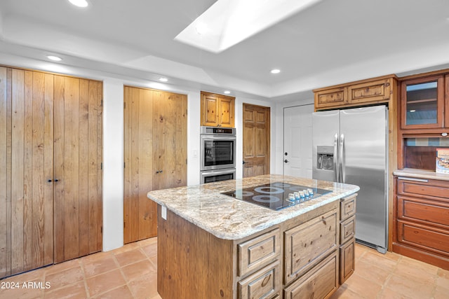 kitchen featuring a skylight, light stone countertops, light tile patterned floors, a kitchen island, and stainless steel appliances