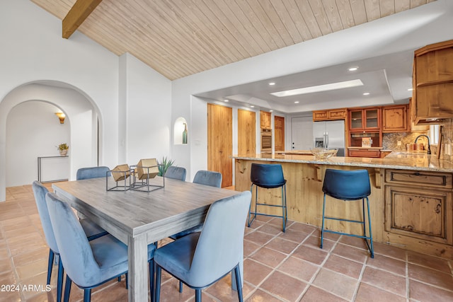 dining space featuring beam ceiling, sink, light tile patterned floors, and wood ceiling