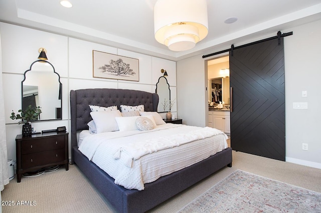 bedroom featuring light carpet, ensuite bathroom, a tray ceiling, and a barn door