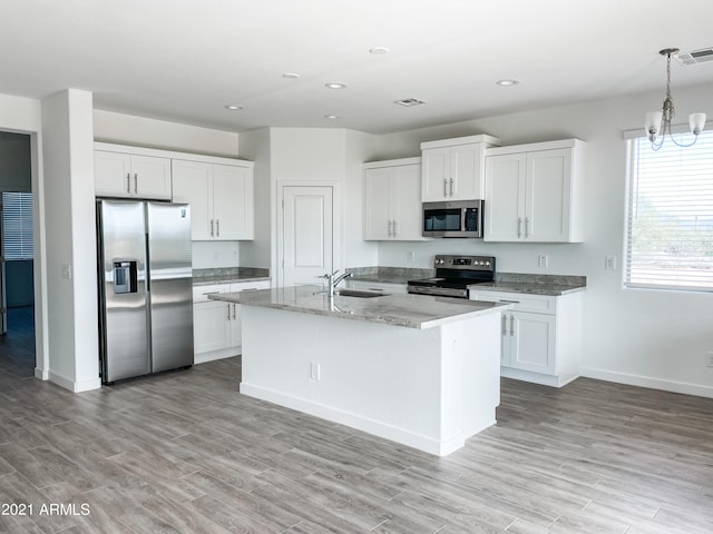 kitchen with stainless steel appliances, hanging light fixtures, an island with sink, and white cabinets