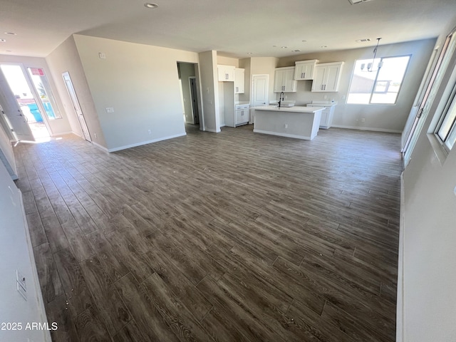 unfurnished living room featuring a notable chandelier, recessed lighting, dark wood-style flooring, a sink, and baseboards