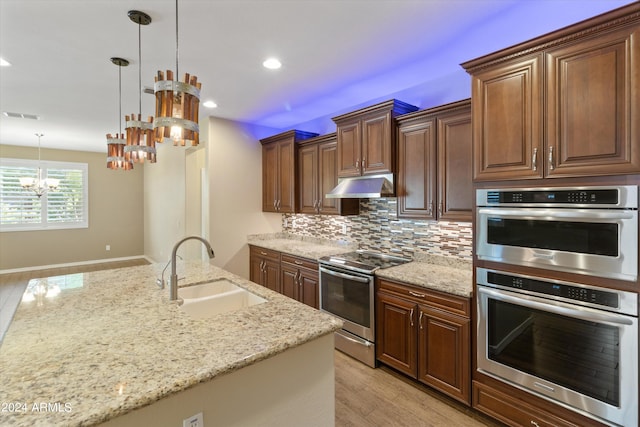 kitchen with appliances with stainless steel finishes, decorative light fixtures, sink, and light wood-type flooring