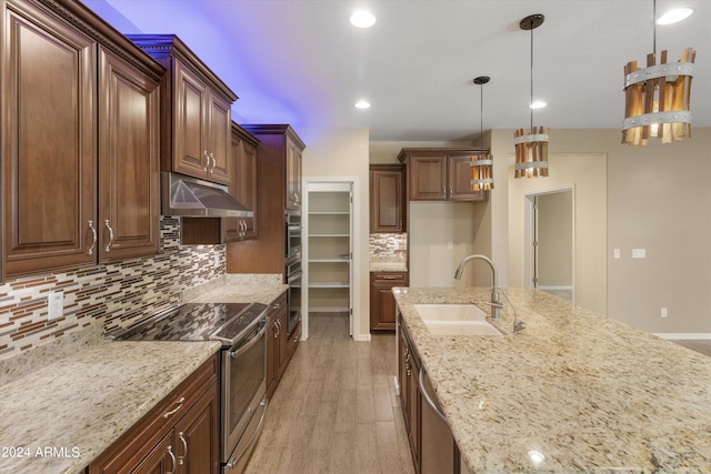 kitchen featuring light stone countertops, sink, stainless steel appliances, pendant lighting, and light hardwood / wood-style flooring