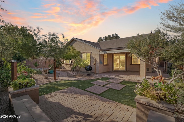 back house at dusk featuring a patio area and a yard