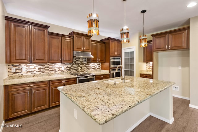 kitchen featuring dark wood-type flooring, hanging light fixtures, stainless steel appliances, a center island with sink, and sink