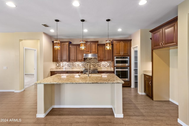 kitchen featuring hanging light fixtures, light stone counters, a center island with sink, and stainless steel double oven