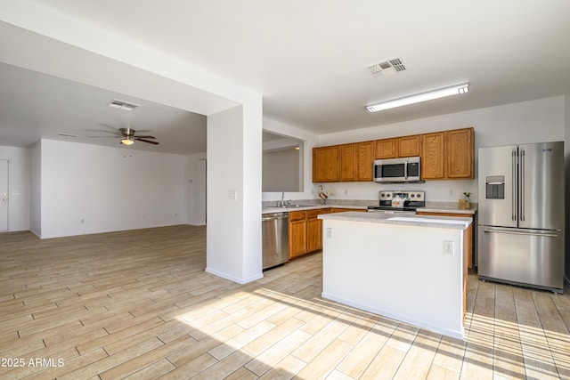 kitchen featuring stainless steel appliances, ceiling fan, sink, light hardwood / wood-style floors, and a kitchen island