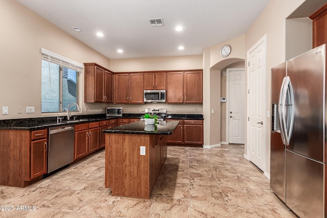 kitchen with appliances with stainless steel finishes, dark stone countertops, a sink, and visible vents