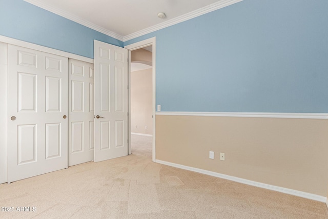 unfurnished bedroom featuring carpet, arched walkways, crown molding, a closet, and baseboards