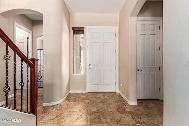 entrance foyer with stairway, baseboards, arched walkways, and stone finish flooring