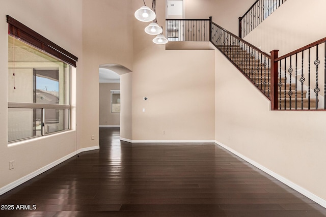 entrance foyer featuring a towering ceiling, baseboards, arched walkways, and wood finished floors