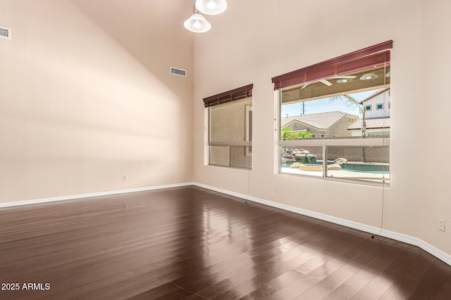 spare room with dark wood-type flooring, visible vents, and baseboards