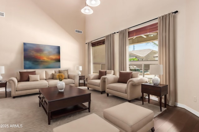 living room featuring a high ceiling, wood finished floors, visible vents, and baseboards