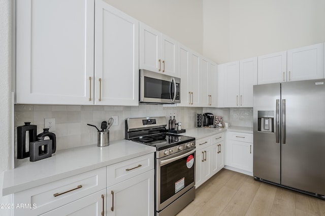 kitchen with white cabinetry, tasteful backsplash, light hardwood / wood-style flooring, appliances with stainless steel finishes, and a high ceiling