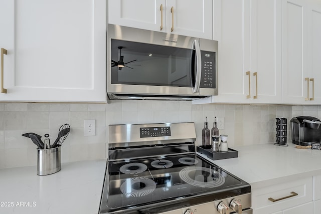 kitchen featuring white cabinetry, light stone counters, ceiling fan, stainless steel appliances, and decorative backsplash