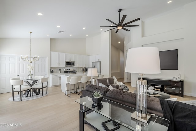 living room featuring high vaulted ceiling, sink, ceiling fan with notable chandelier, and light hardwood / wood-style flooring