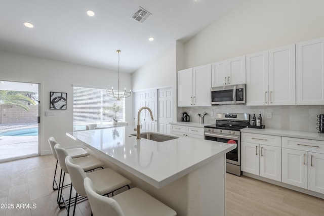 kitchen featuring sink, stainless steel appliances, decorative light fixtures, and a kitchen island with sink