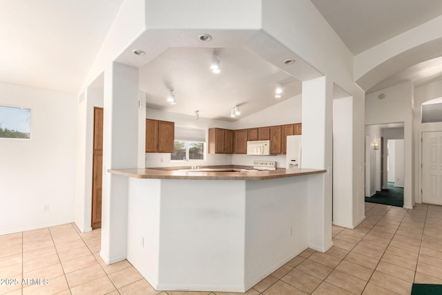 kitchen with brown cabinetry, white appliances, arched walkways, light tile patterned floors, and vaulted ceiling