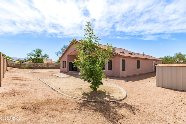 rear view of property with a storage shed, an outbuilding, fence, a patio, and stucco siding
