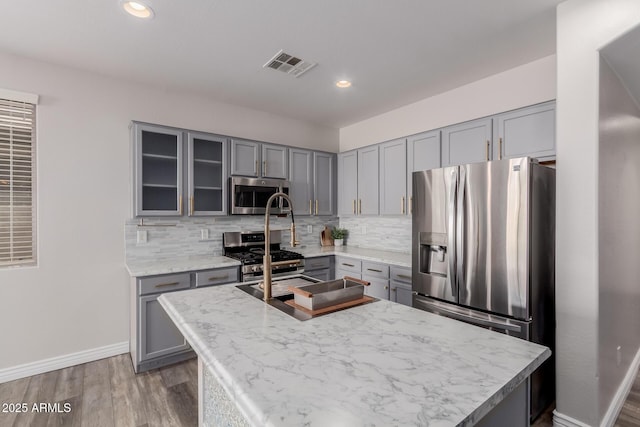 kitchen with tasteful backsplash, hardwood / wood-style flooring, stainless steel appliances, and a center island with sink