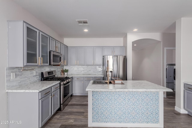 kitchen with washer / clothes dryer, sink, light stone counters, stainless steel appliances, and a center island with sink