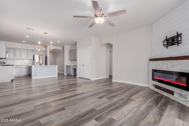 unfurnished living room featuring wood-type flooring, a stone fireplace, and ceiling fan with notable chandelier