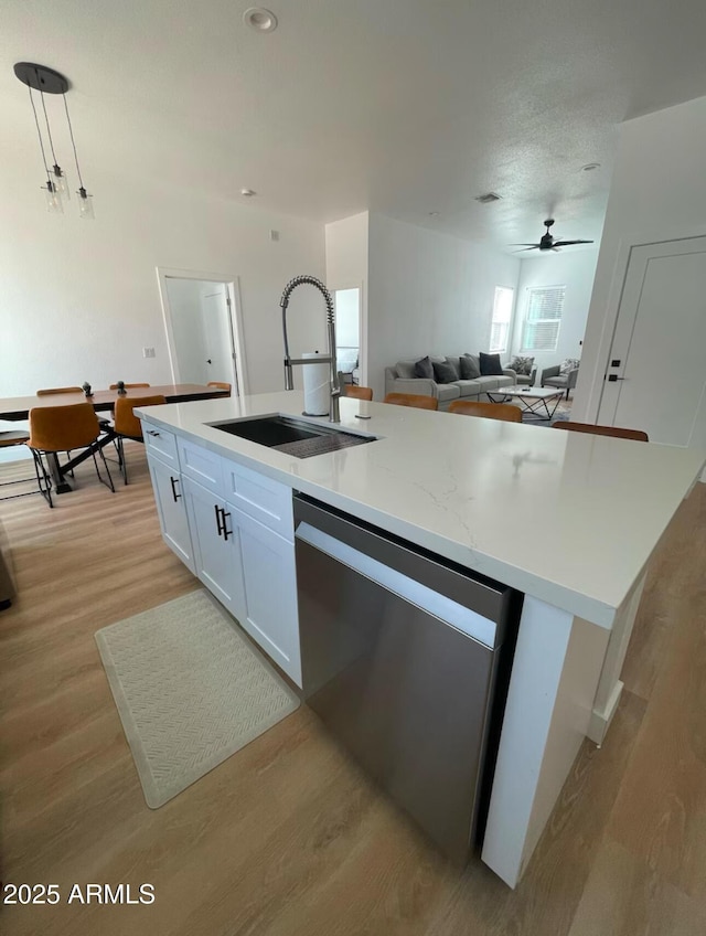 kitchen featuring a sink, white cabinetry, light wood-style floors, dishwasher, and a center island with sink